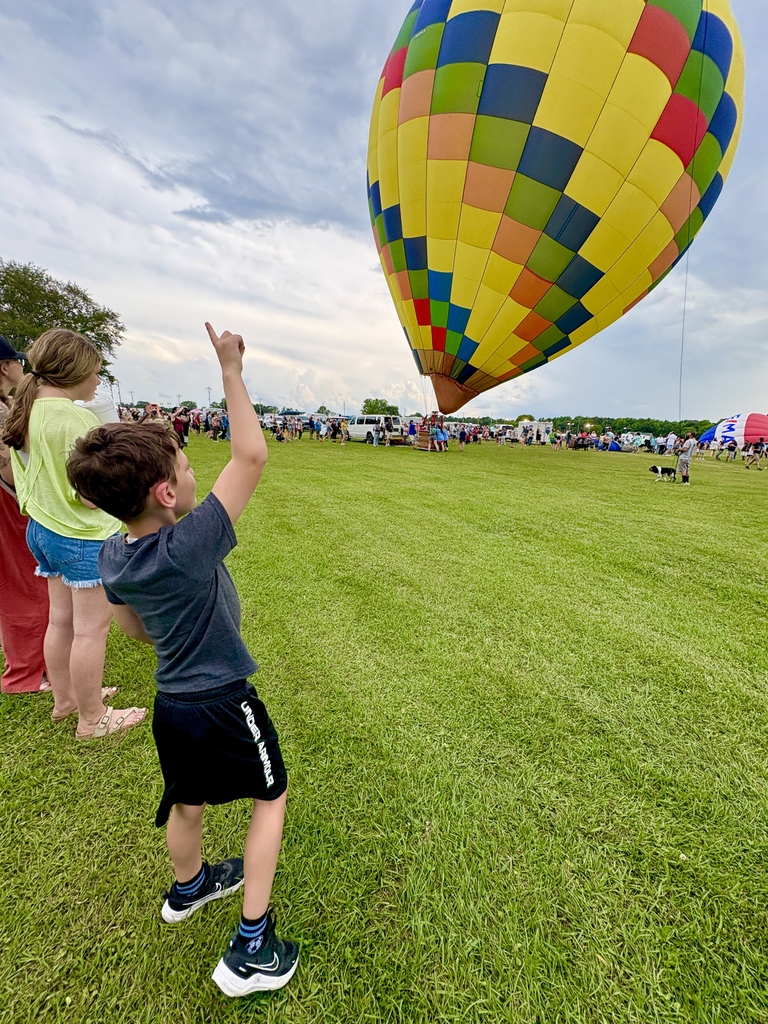 A boy points toward the sky while watching a hot air balloon inflate in a field.