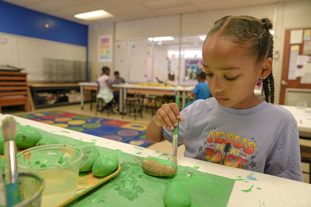 A student paints a rock while inside a classroom.