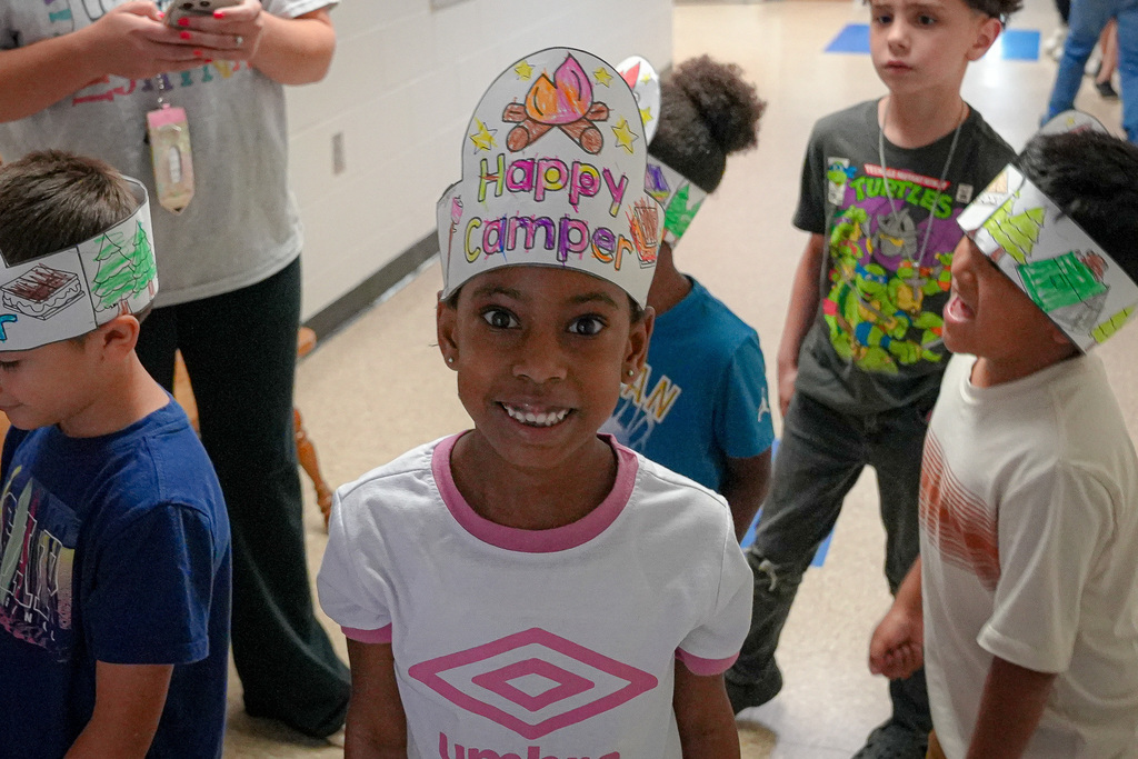 A girl smiles and wears a hat made out of paper that says "happy camper."