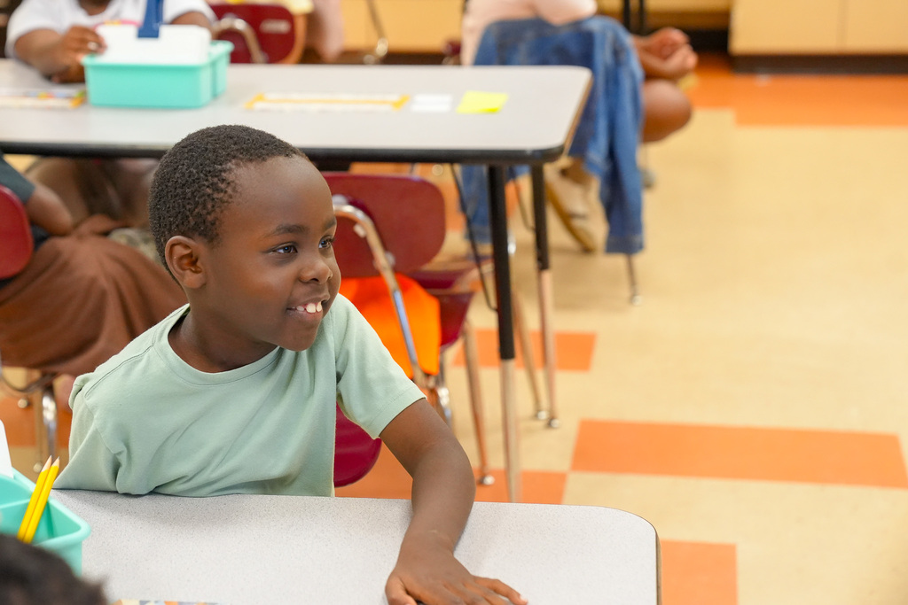 A student smiles while sitting at a desk inside a classroom.