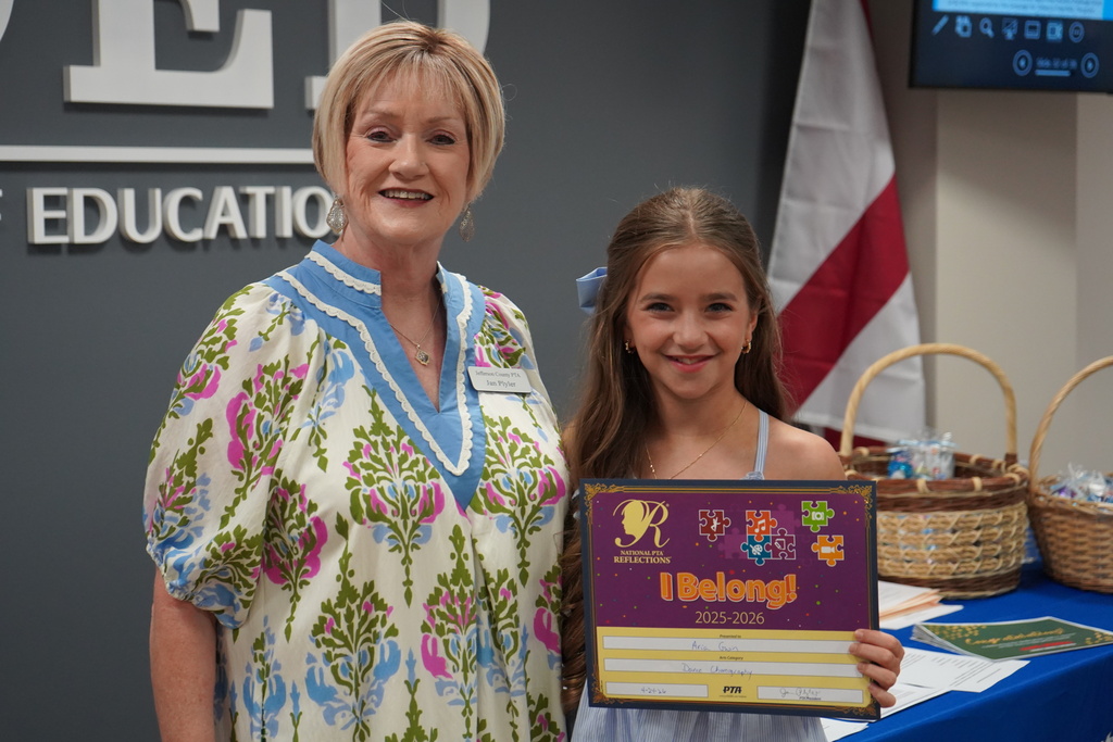 A woman and a JEFCOED student smile and pose for a photo inside a room in the Jefferson County Schools Board of Education. The girl holds a certificate in her hands. 