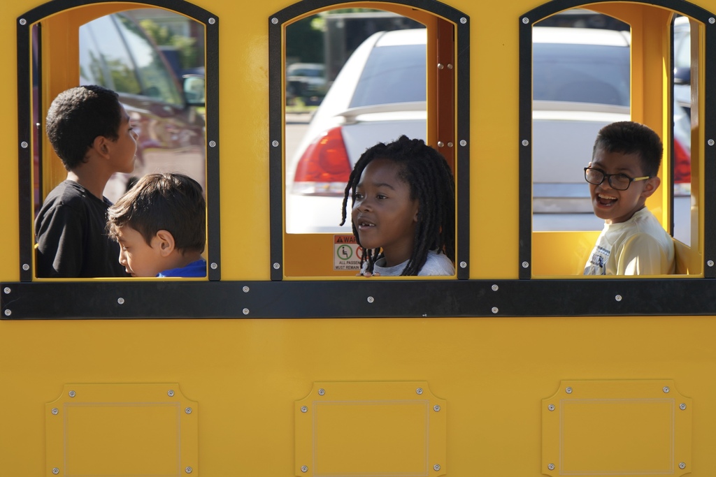 Students smile while riding inside a carnival-style train inside a parking lot.