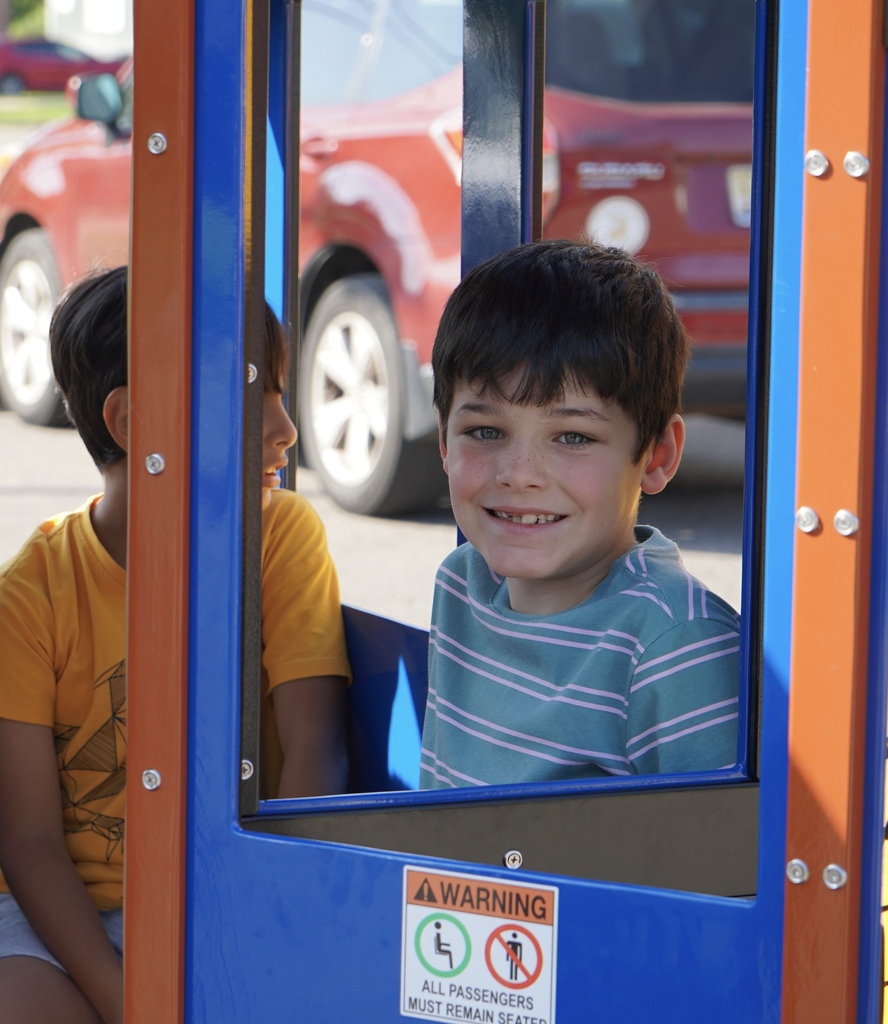 A student smiles while sitting in a train car inside a school parking lot.