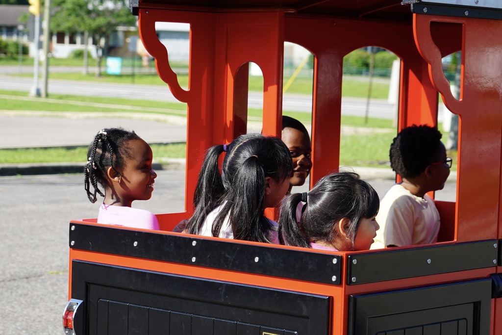 Students smile while riding in a red train car.