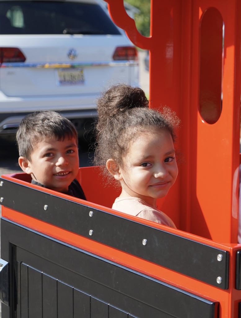 Two children smile while sitting inside a carnival-style train.