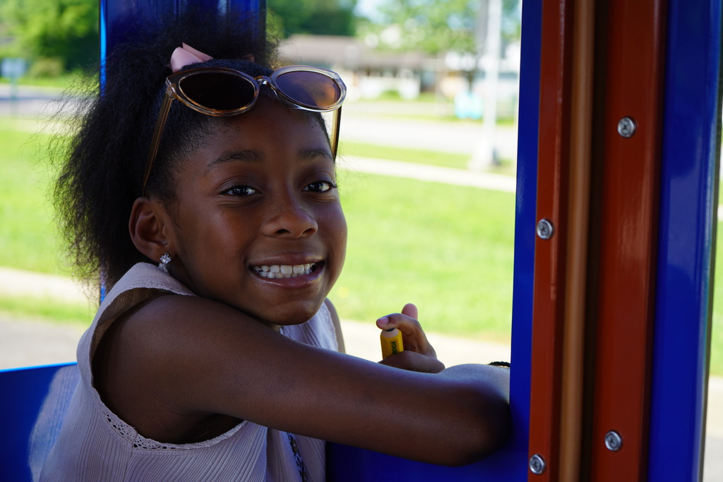 A girl smiles while riding inside a blue train car.