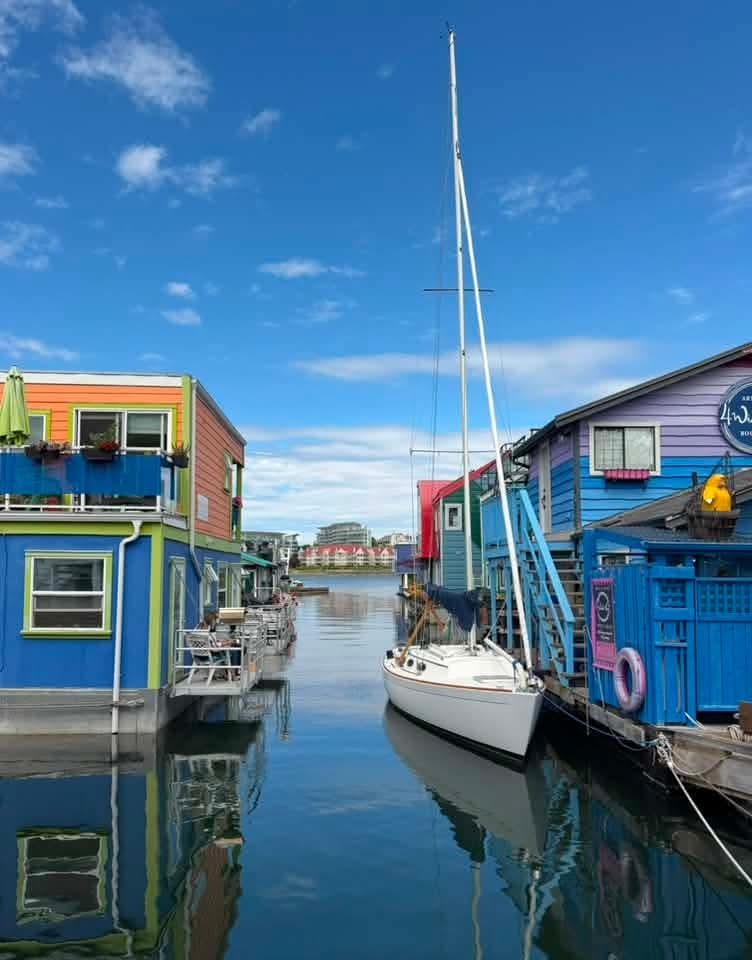Brightly colored buildings sit on a large body of water. A sailboat floats next to the buildings.