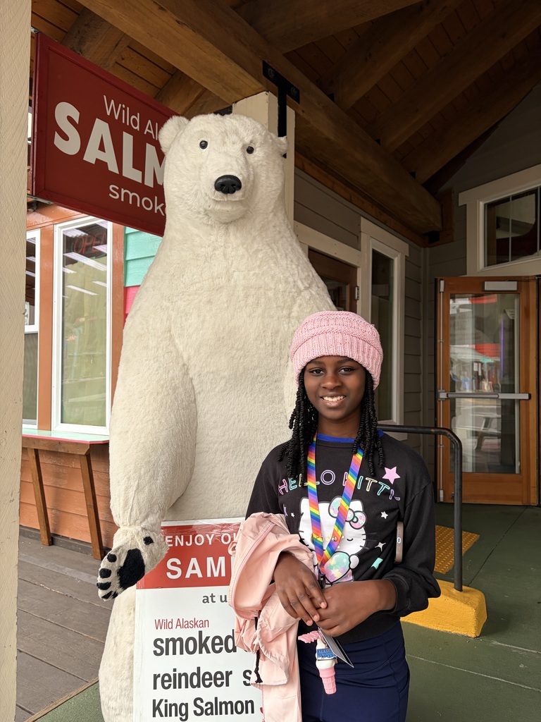 A girl smiles while standing in front of a polar bear statue at a general store.