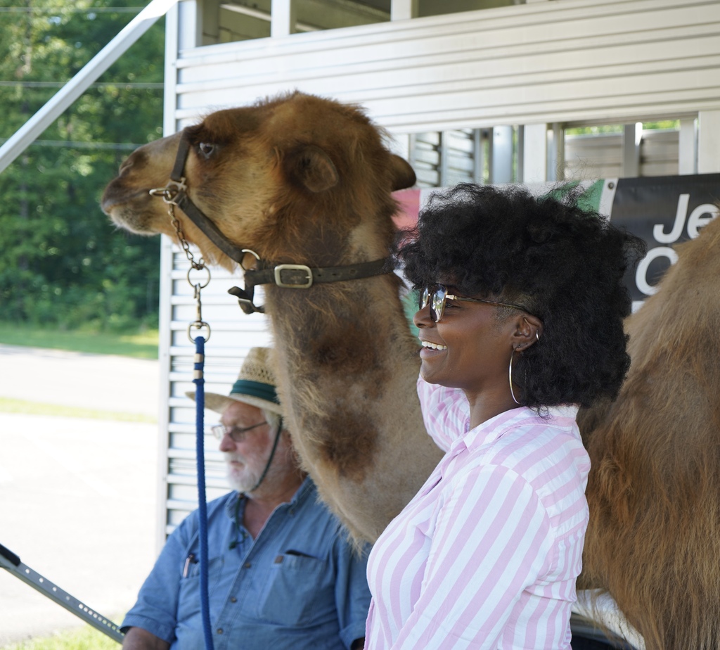 A teacher smiles for a photo with a camel.
