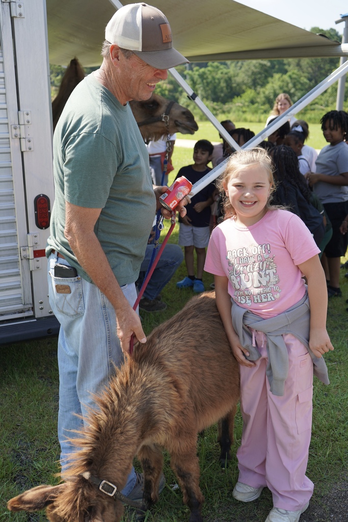 A girl smiles for a photo with a baby donkey. A man stands nearby holding a leash that's attached to the donkey.