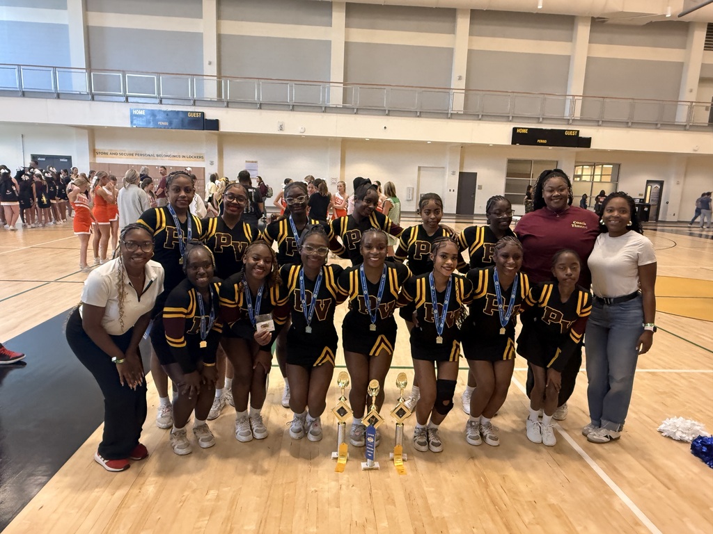 Pinson Valley High School cheerleaders pose for a photo inside a gym. They smile and stand behind awards that are sitting on the ground. The cheerleaders in the front of the photo wear medals around their necks.