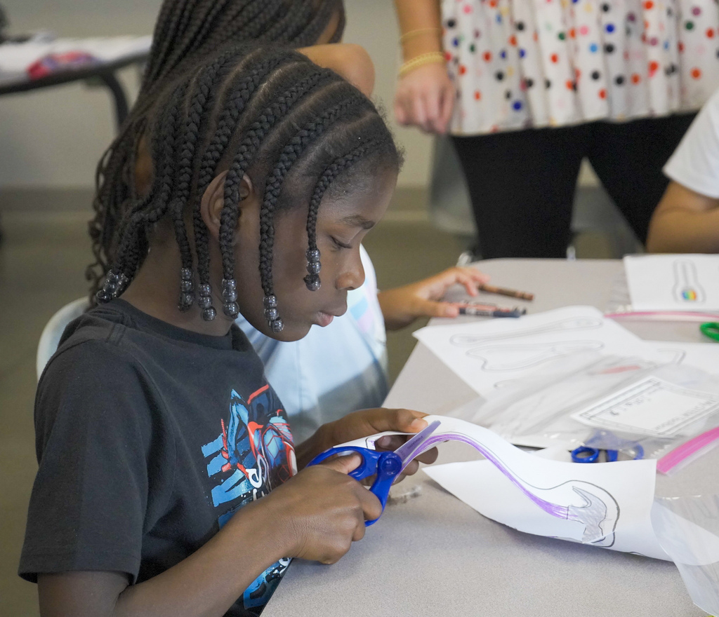 A student sits at a desk and cuts out a piece of paper.