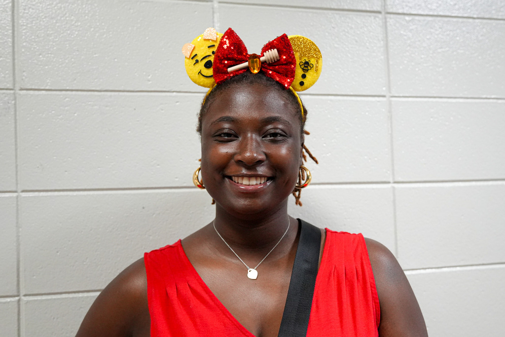 A woman wearing Winnie the Pooh-themed Disney ears smiles for a photo.