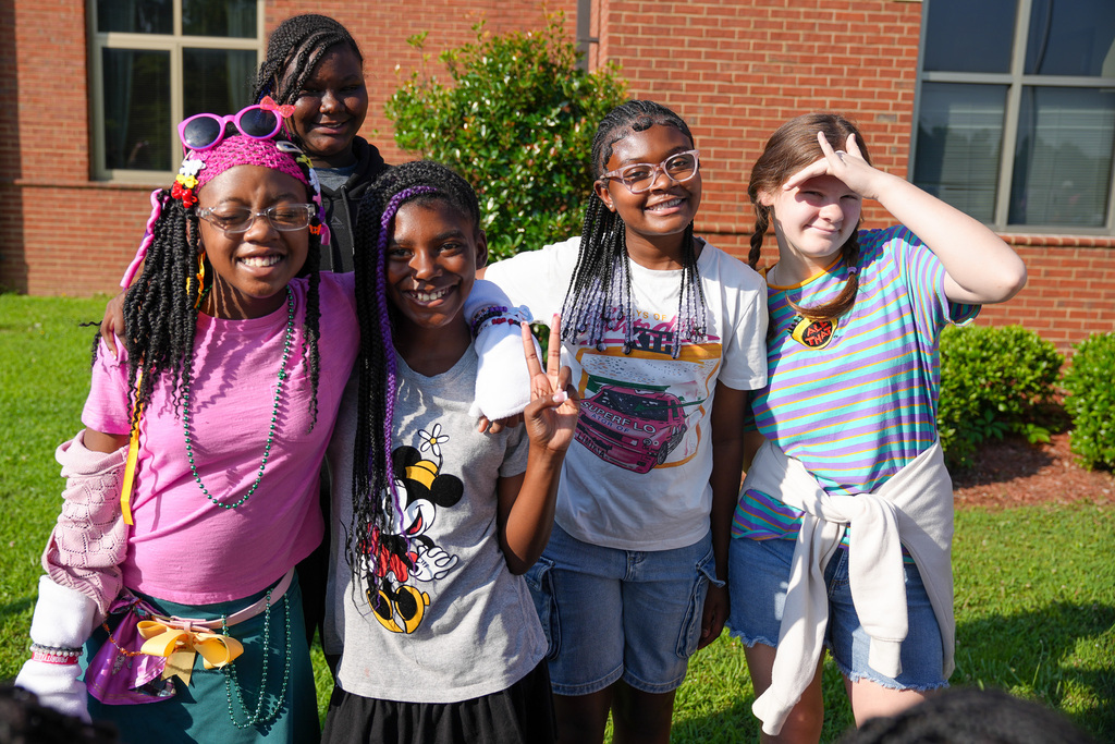 A group of girls wearing Disney-themed outfits stand outside a school and smile for a photo.