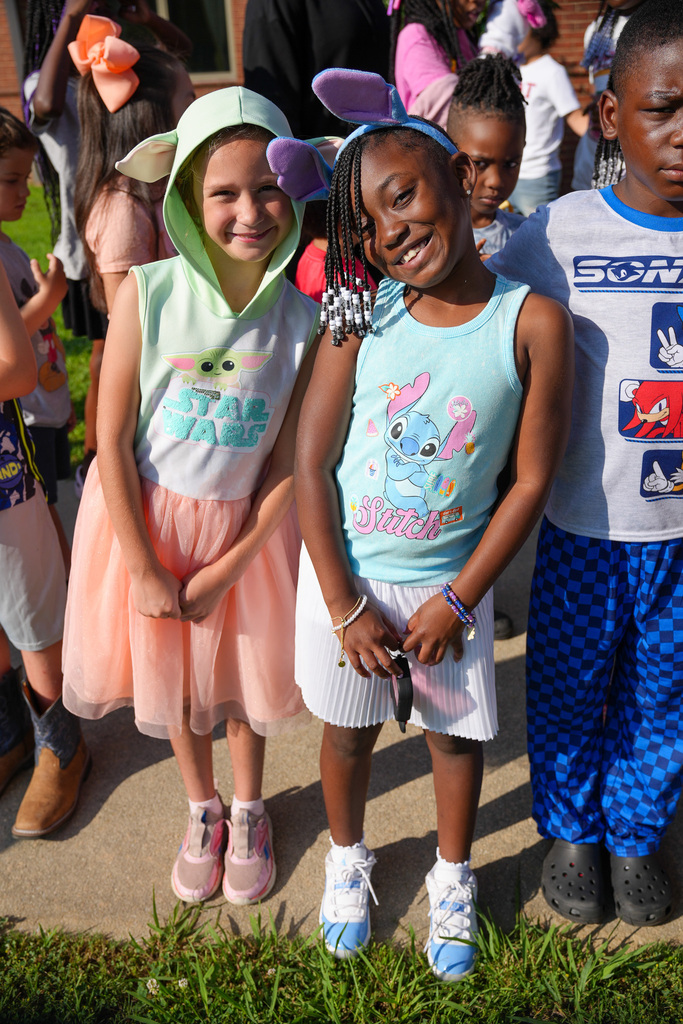 Two girls stand together outdoors and smile. One of the girls wears a Star Wars themed hoodie with Yoda ears on the hood. The other girl wears a Stitch themed shirt and a head band with Stitch ears.