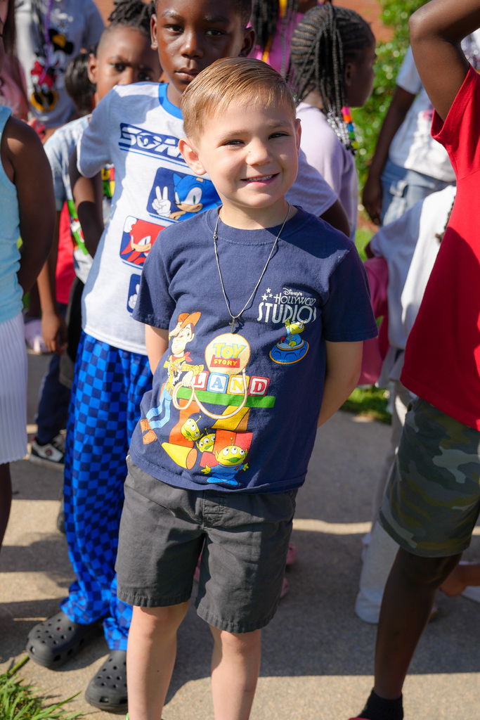 A boy wearing a Toy Story shirt stands outdoors and smiles for a photo.
