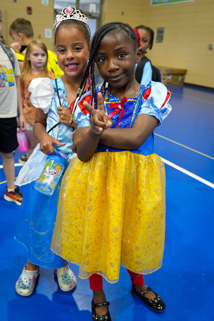 Two girls wearing princess costumes smile for a photo inside a school gym.