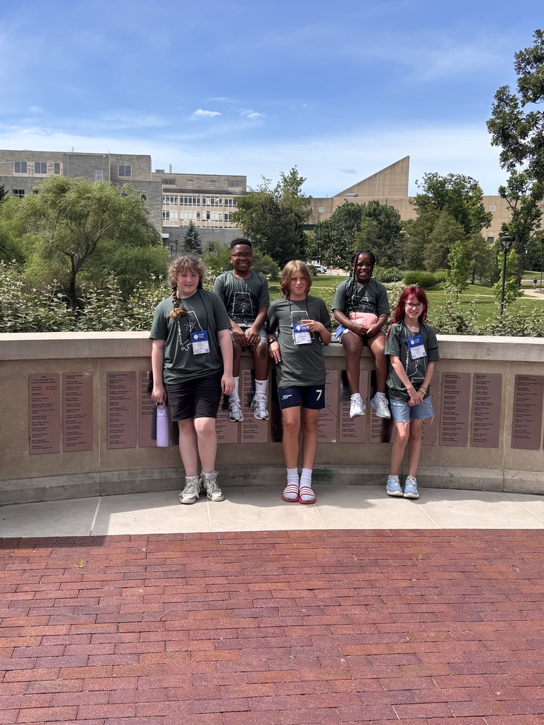 A group of students wearing matching gray shirts with an outline of the state of Alabama on them pose for a photo outdoors on a college campus.
