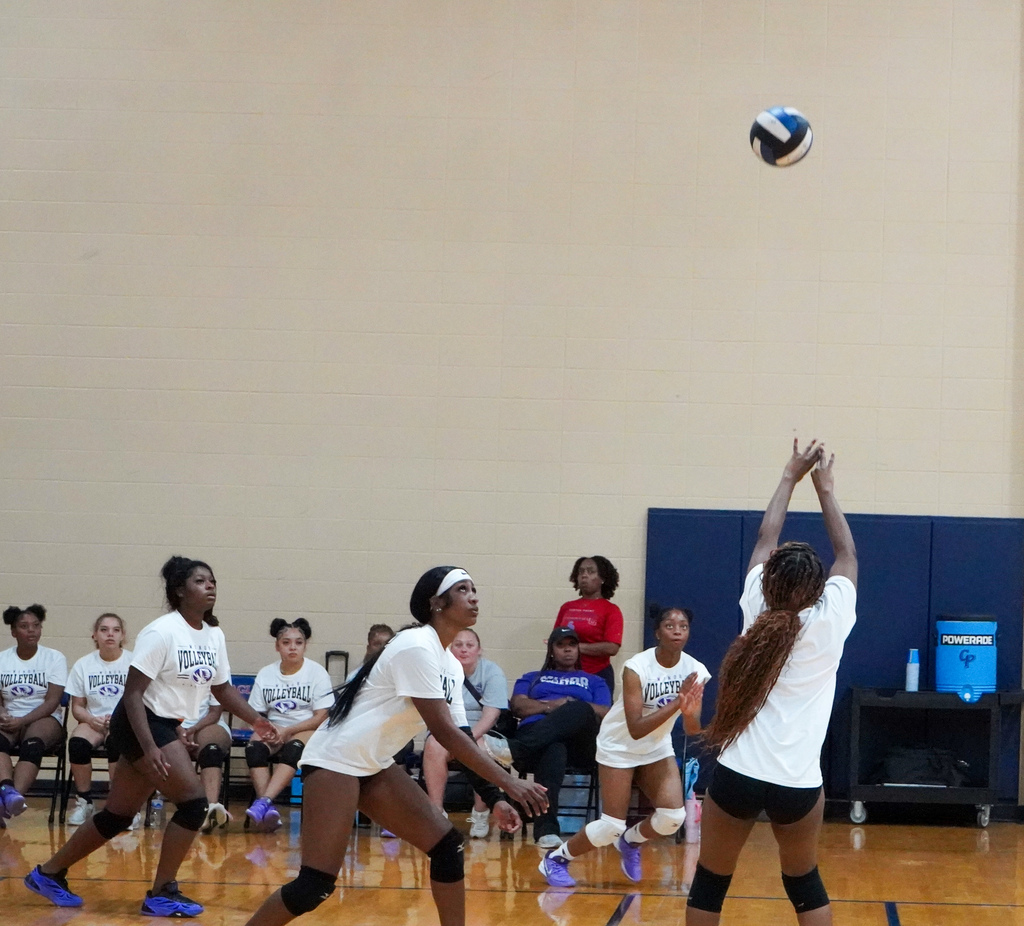 A Minor High School volleyball player sets the ball during a game inside a school gym.