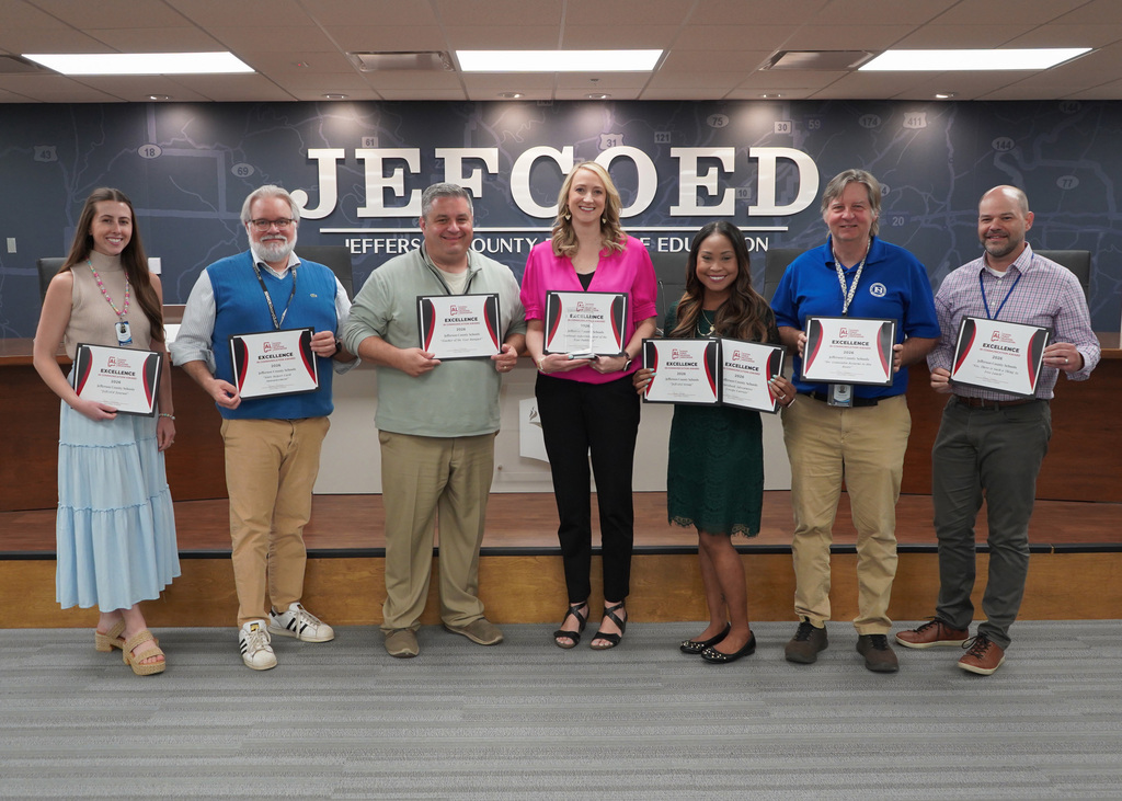 Members of the Jefferson County Schools communications department pose for a photo inside the JEFCOED board room. They hold certificates in their hands.
