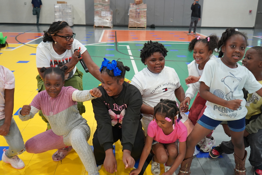 Students and a teacher dance during a performance inside a school gym.