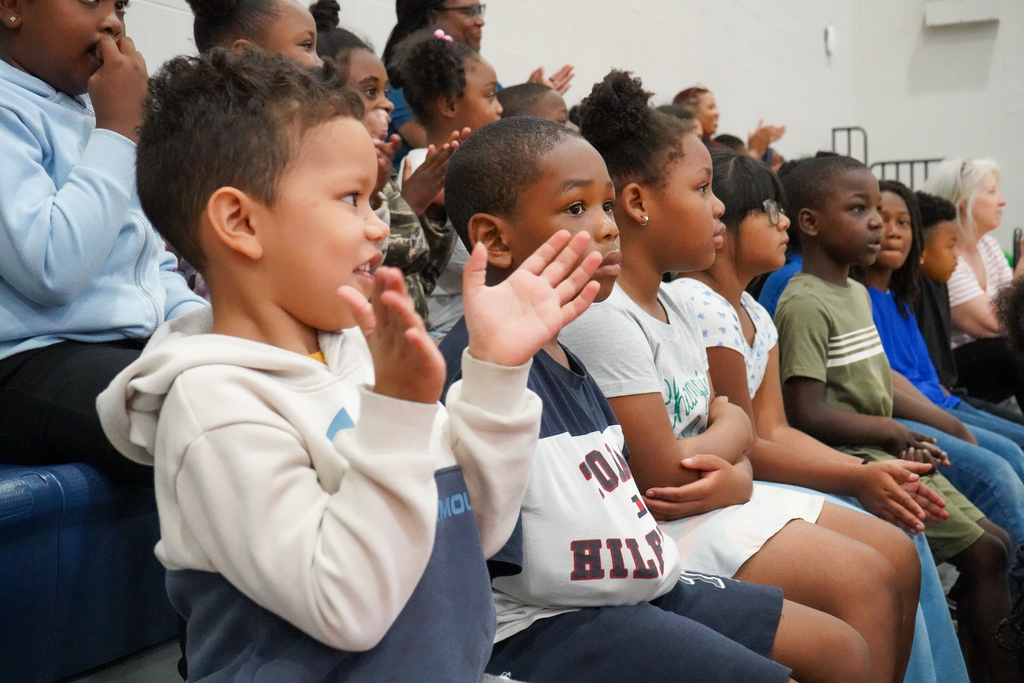Students clap while watching a performance inside a school gym.