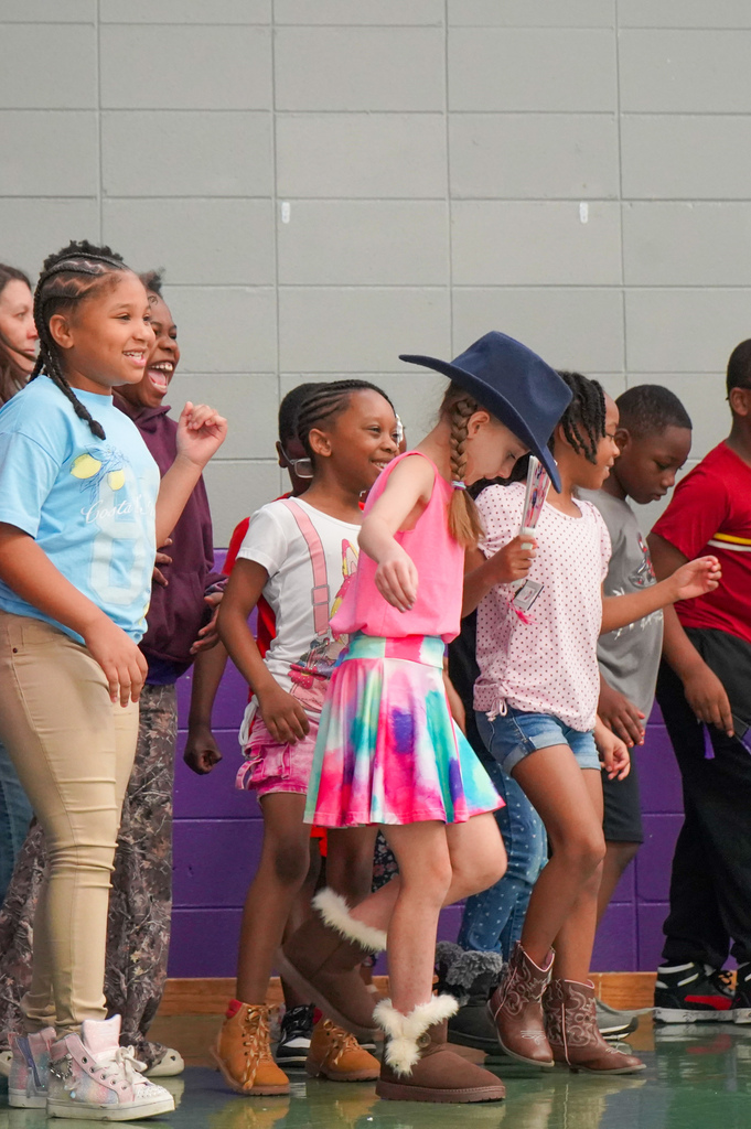 Students wearing western boots and hats dance on a stage.
