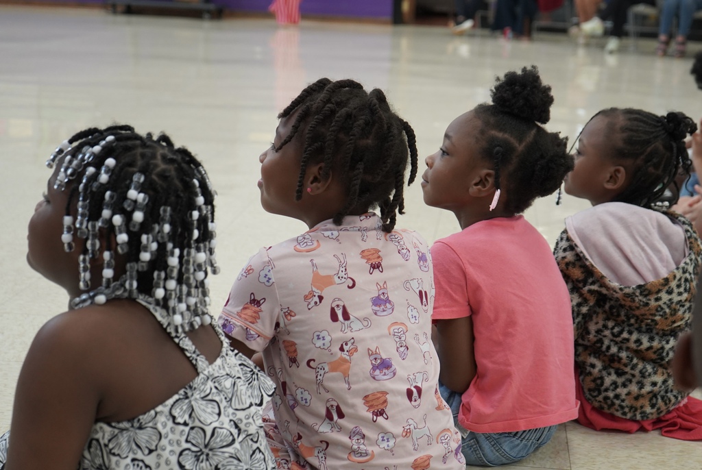 A group of girls sit on the floor and watch a performance.