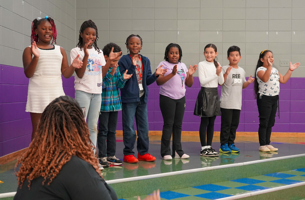 Students stand on a stage and clap their hands and sing.