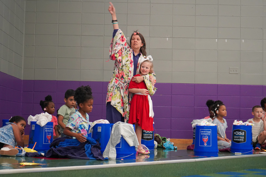 A teacher and students perform a musical number to a song from "Annie". Students sit on the floor next to cleaning buckets, and a teacher dressed like Ms. Hannigan hugs a student dressed like Annie.