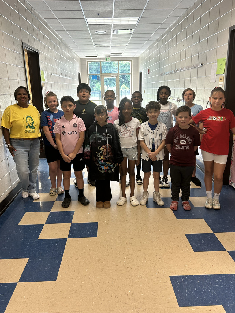 Students and a teacher pose for a photo in a school hallway. They all wear different outfits supporting their favorite World Cup teams.