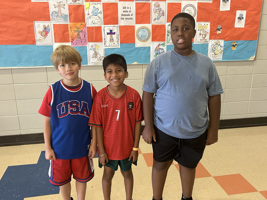 Students stand in a school hallway and smile for a photo. They wear outfits celebrating their favorite teams in the World Cup.