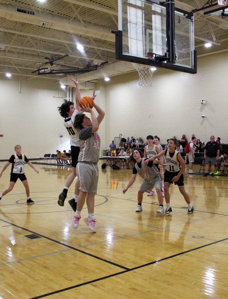 Two players jump in the air during a basketball game. One of the players blocks the other player as he shoots  