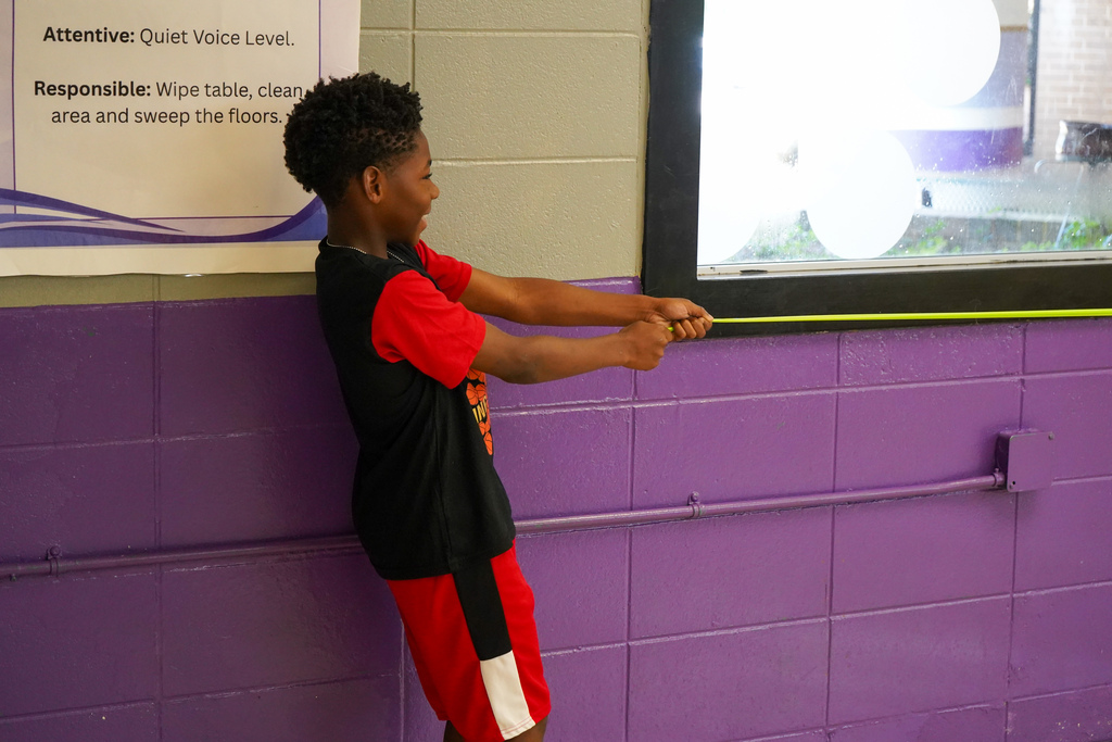 A student smiles while standing inside a lunch room and holding a long piece of elastic.
