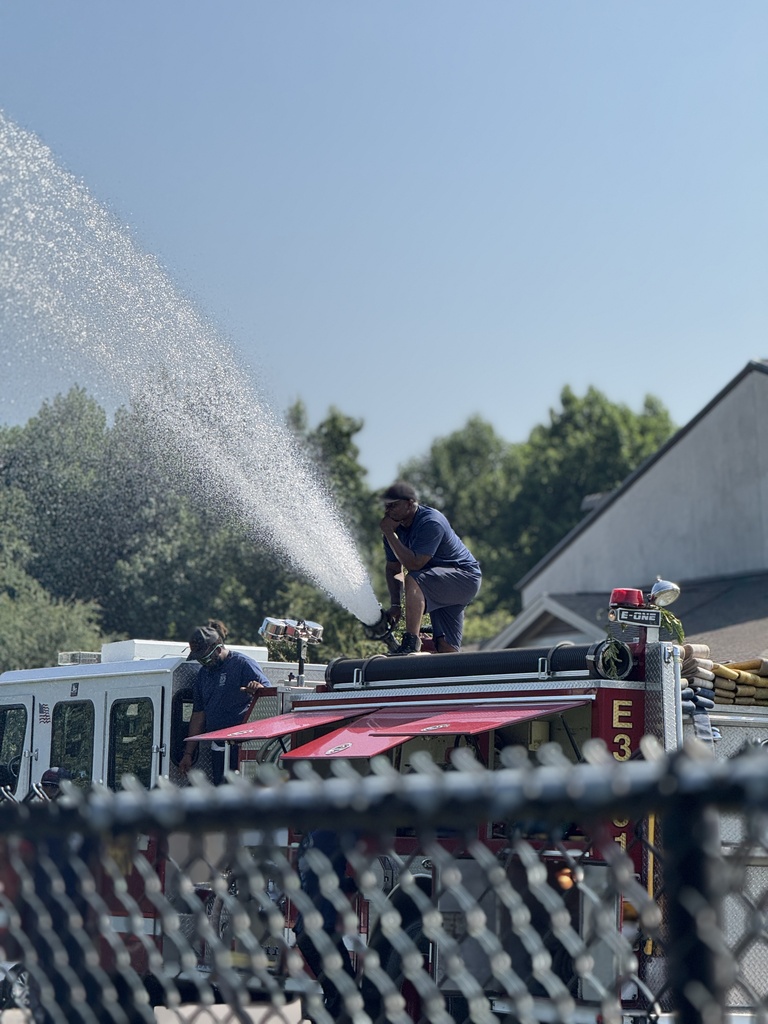 A firefighter sprays water from his fire truck for children to play in outdoors.