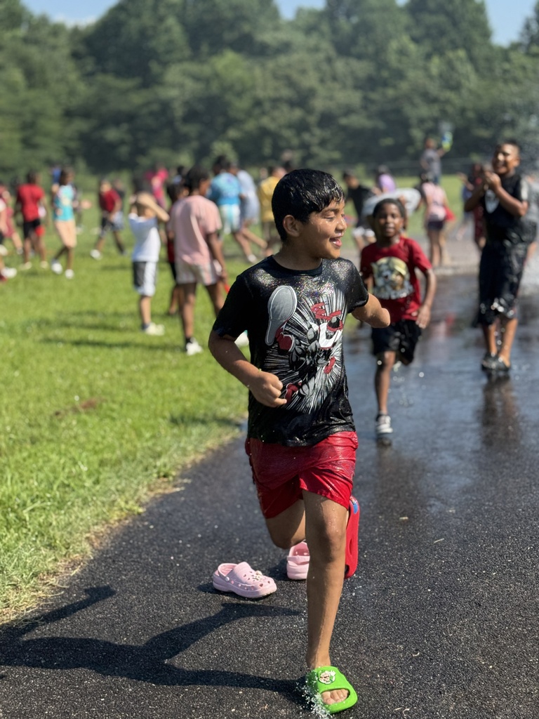 A child smiles while running through water that's being sprayed through the air outdoors.
