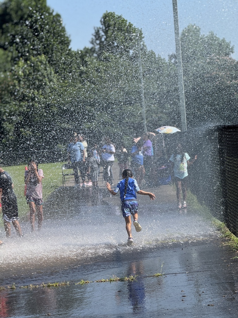 A child runs through water as it's being sprayed through the air outdoors.