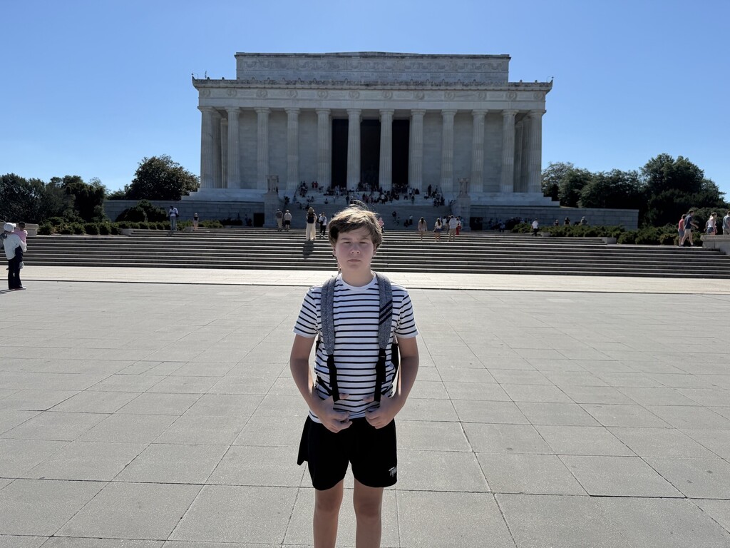 A boy smiles for a photo while standing in front of the Lincoln Memorial.