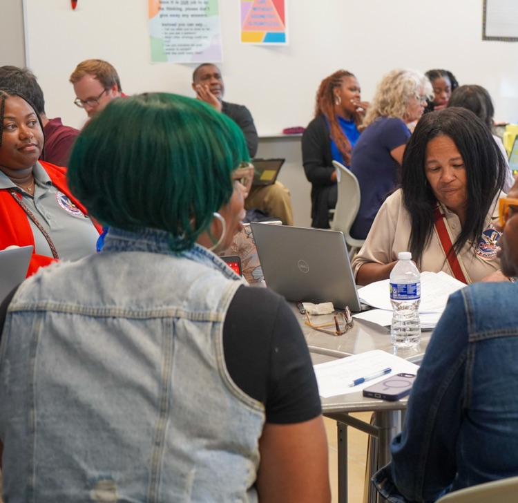 Educators and administrators sit at desks inside a classroom  