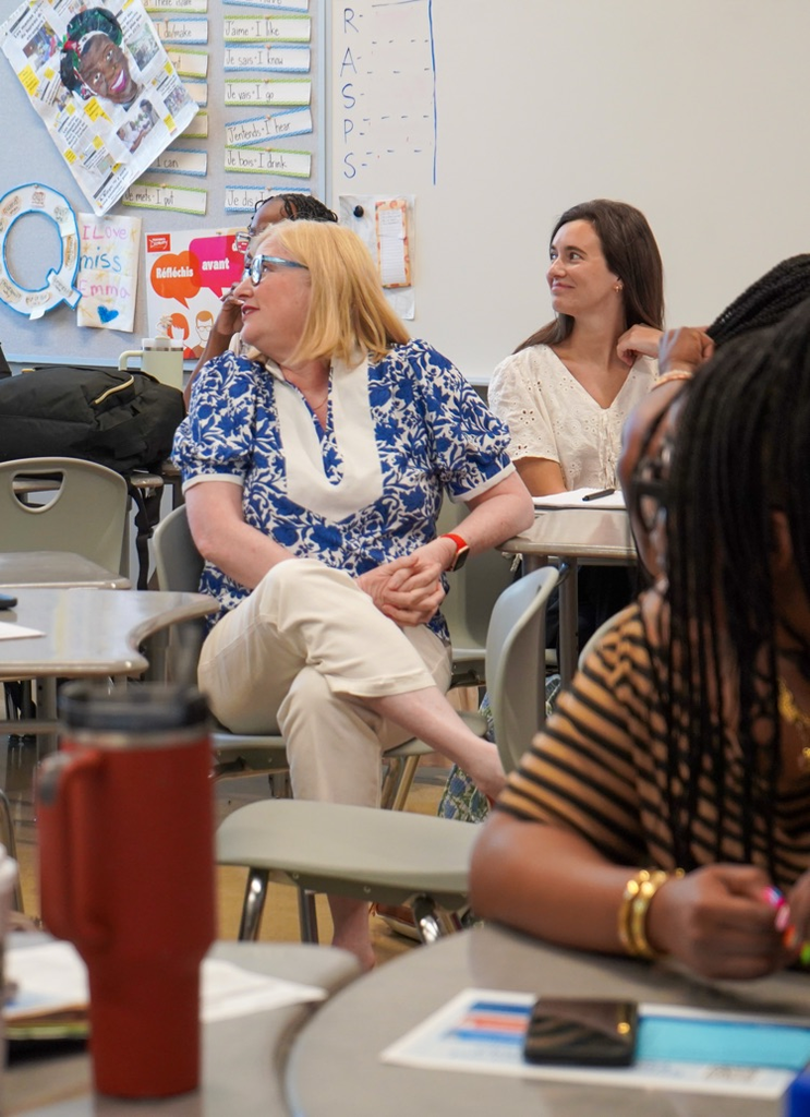 Educators smile while sitting at desks in a classroom during professional development  