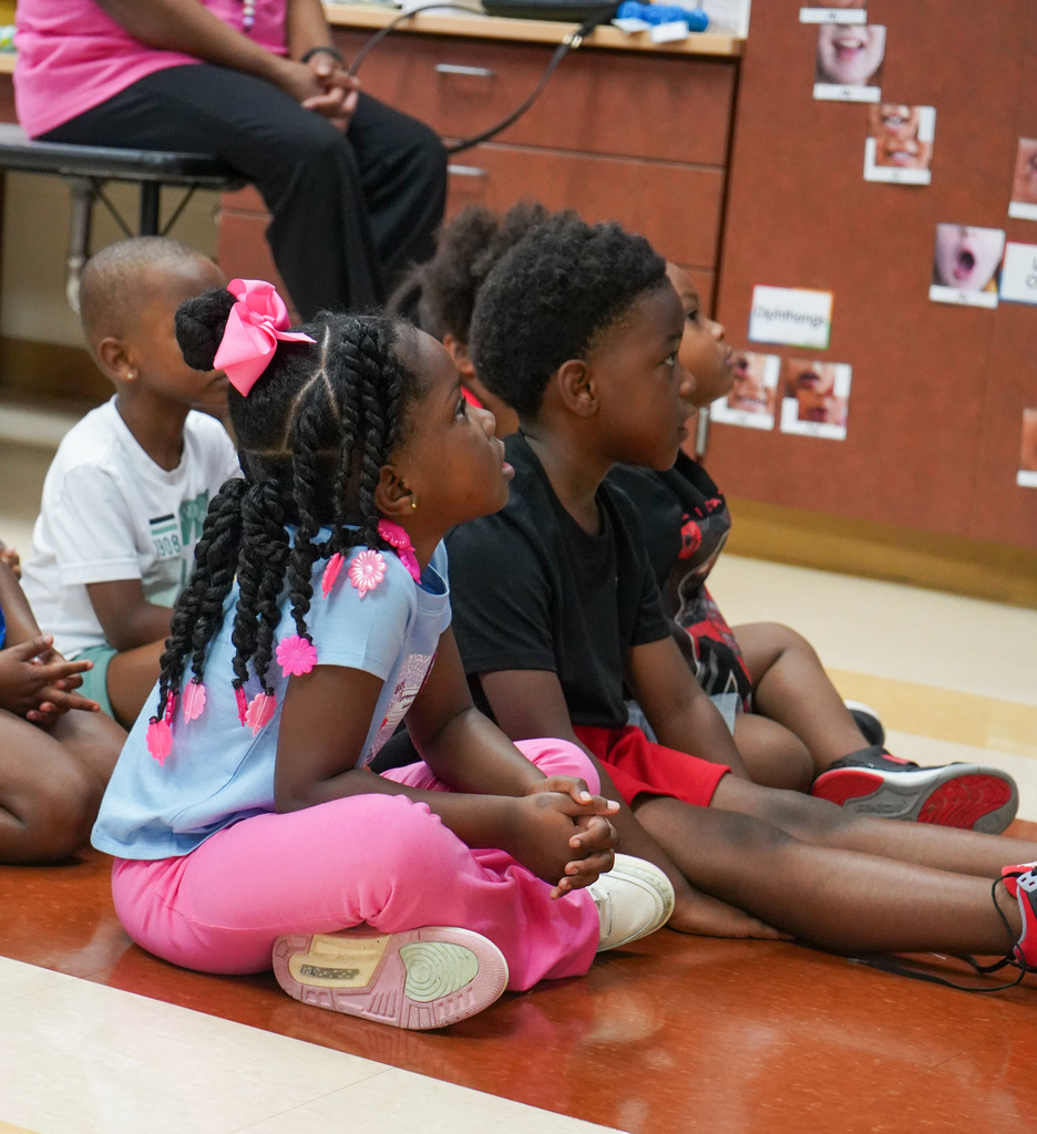 Children sit on the floor of a classroom and listen during a lesson.