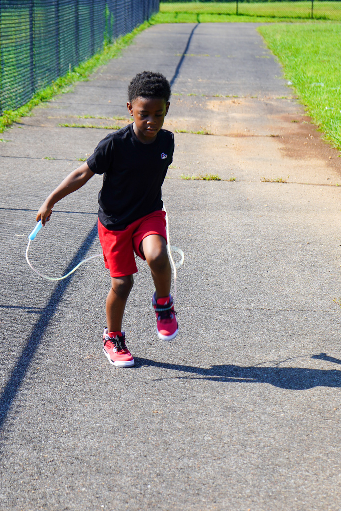 A boy jump ropes down the sidewalk while playing outside.