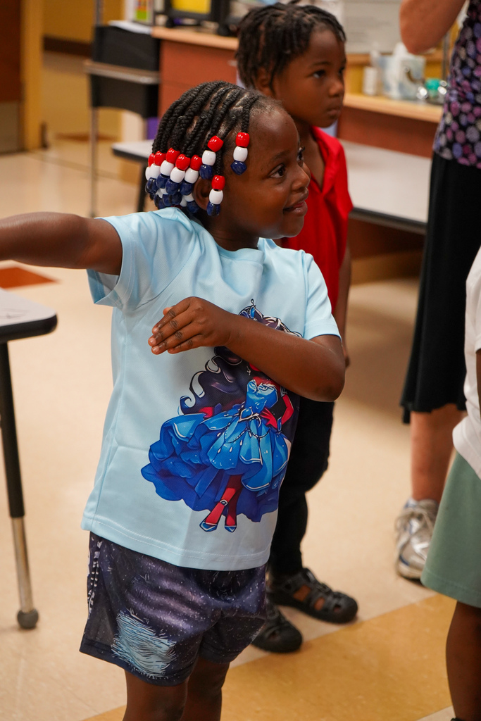 A girl dances and smiles while standing inside a classroom.