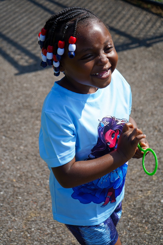 A girl smiles while standing on a sidewalk outside.