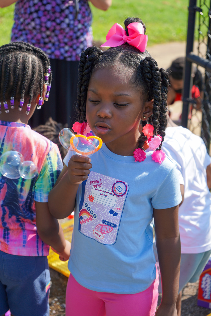 A girl blows bubbles while standing outside.
