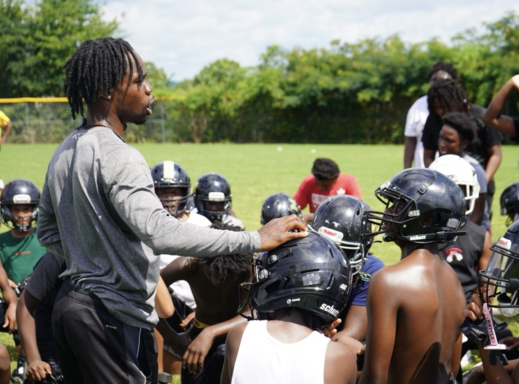 A football coach talks to his players while they sit on a grassy field in a huddle