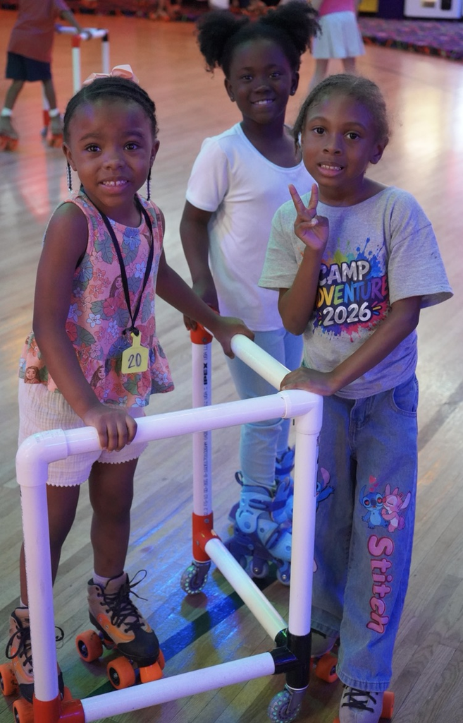 Three girls smile for a photo at a skating rink. One of them holds onto a walker