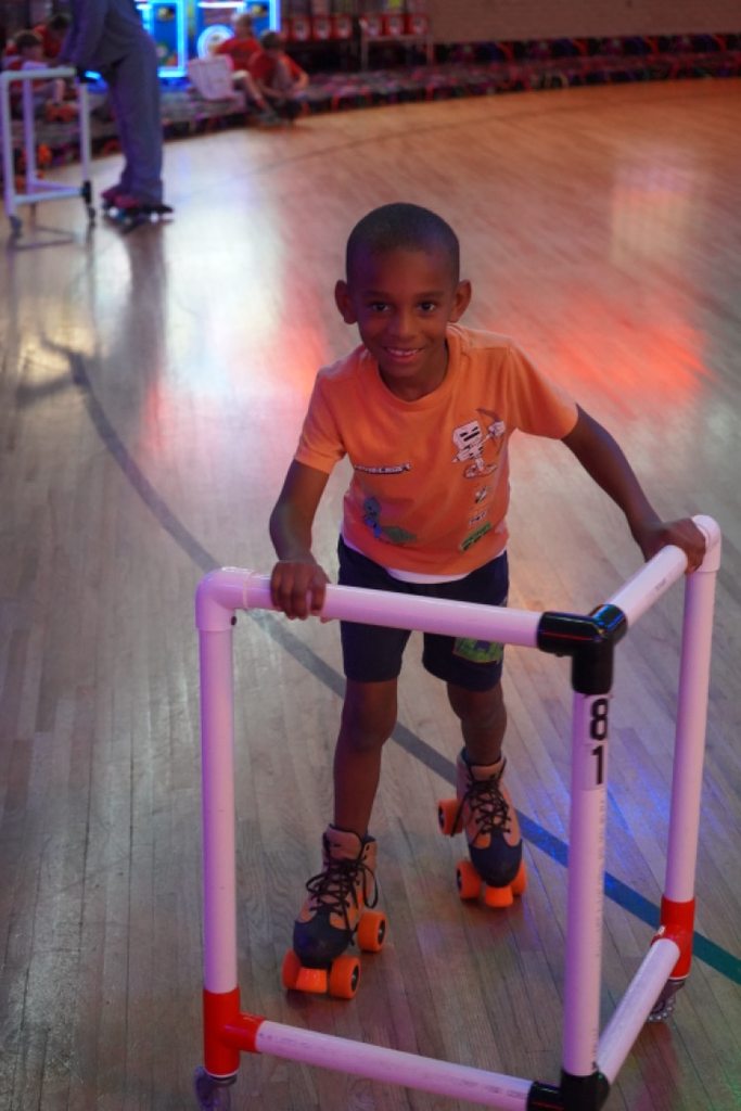 A boy smiles while skating with a walker at a skating rink
