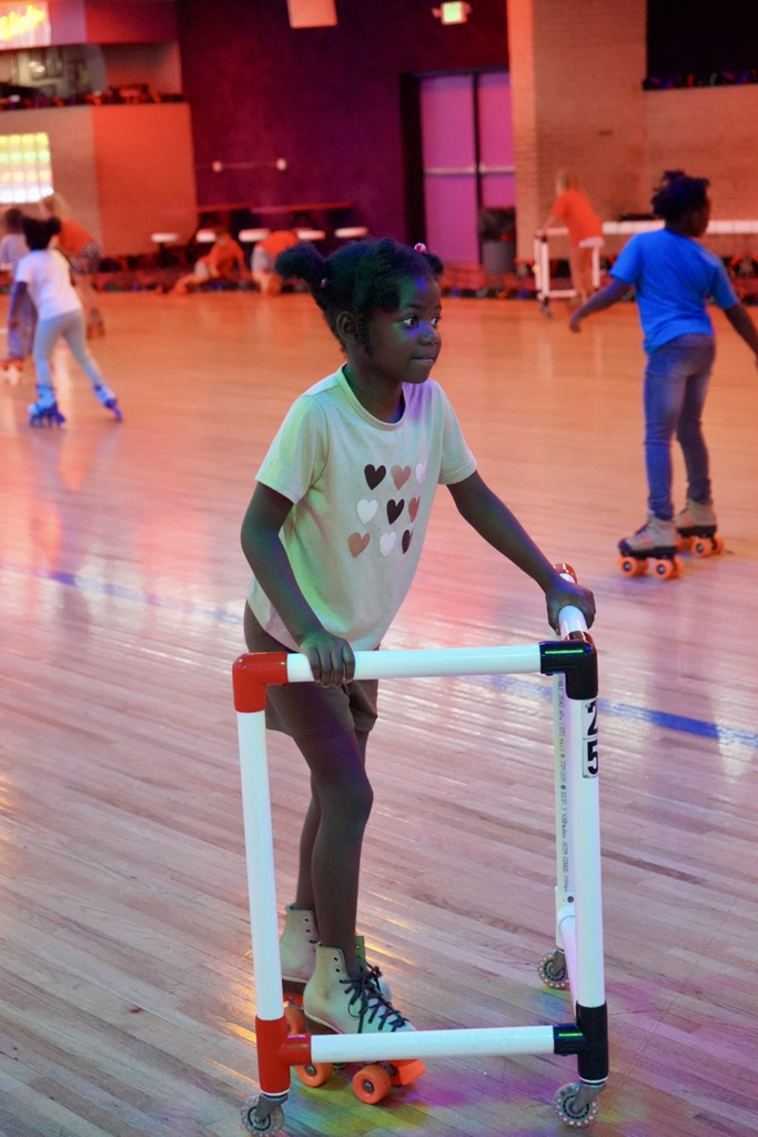 A girl smiles while skating with a walker at a skating rink