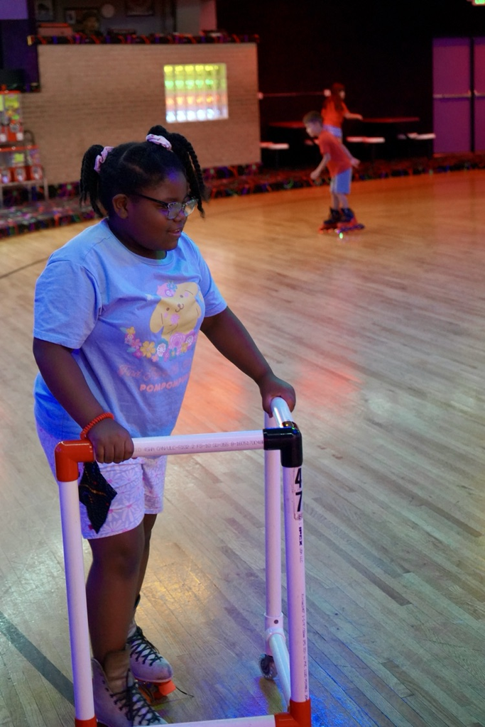 A girl holds a walker and skates across the floor at a skating rink